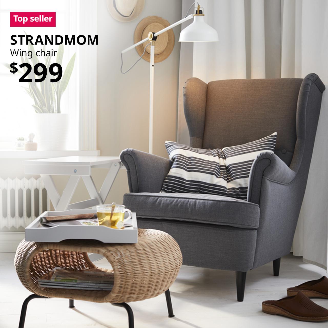 A nordvalla dark grey STRANDMOM wing chair at the corner of the living room next to the window. A red "Top seller" label is on the top left of image, with black text below that reads: STRANDMOM, Wing chair. Price $299"