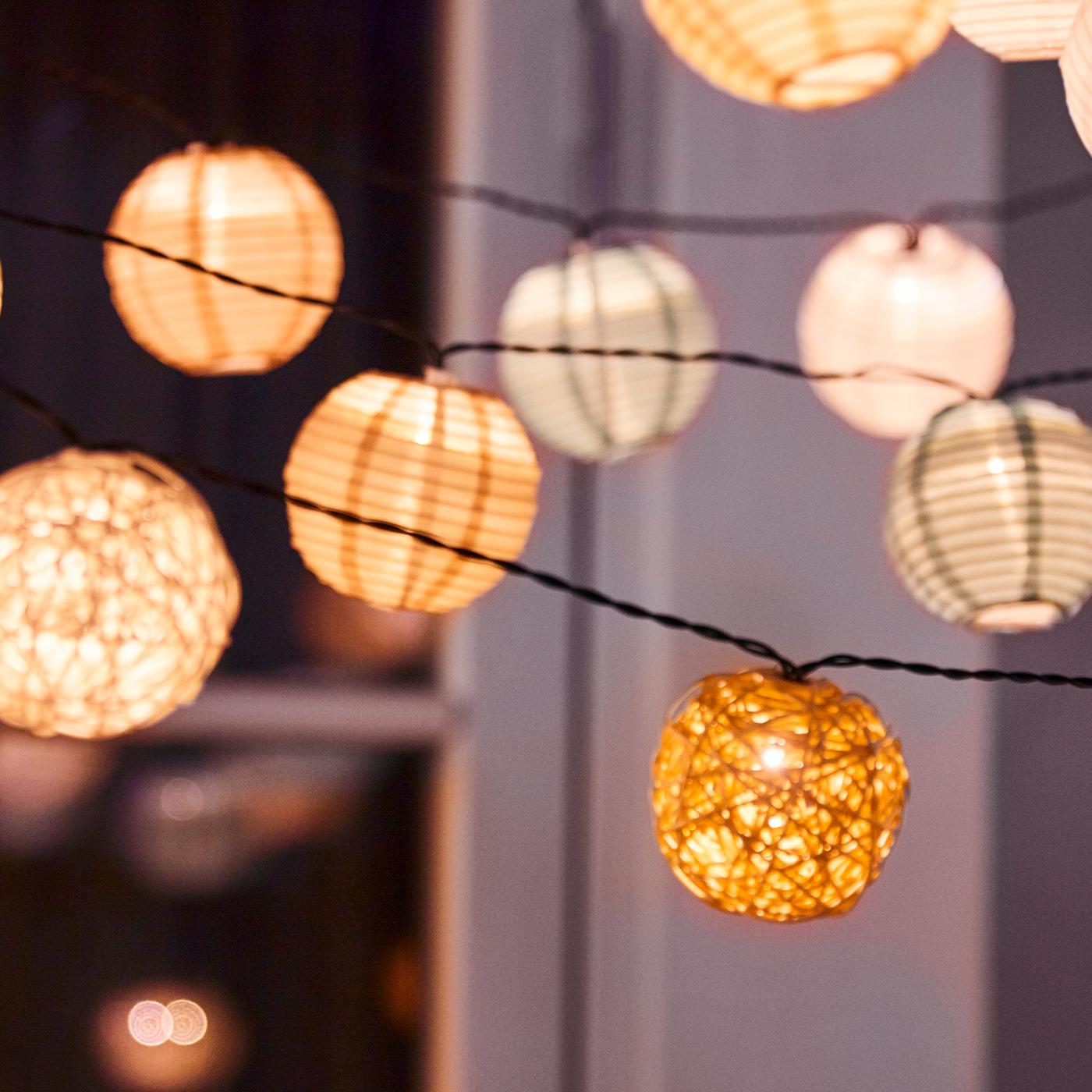 A number of different types of LED lighting chains hang outside a window. The lighting chains are lit.