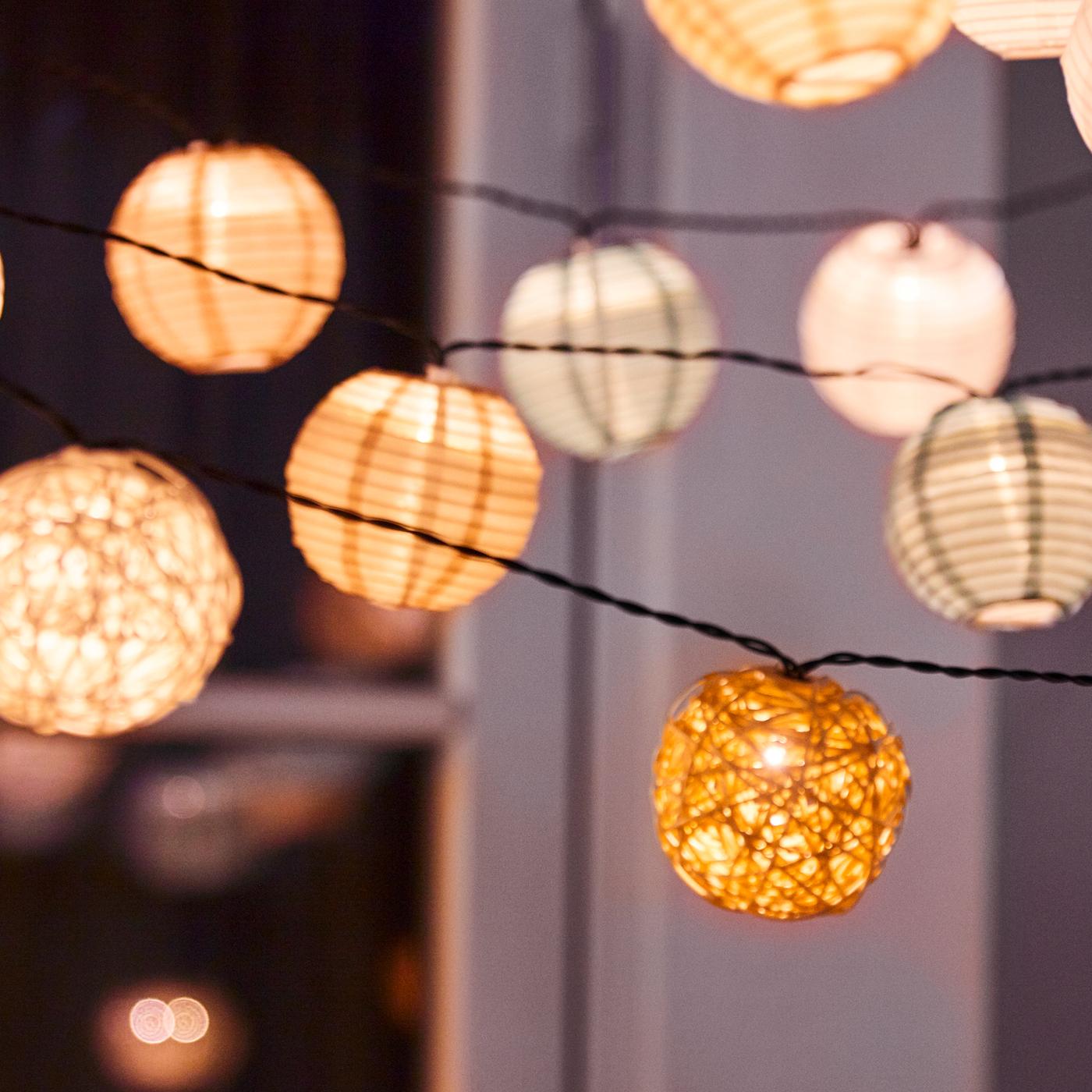 A number of different types of LED lighting chains hang outside a window. The lighting chains are lit.