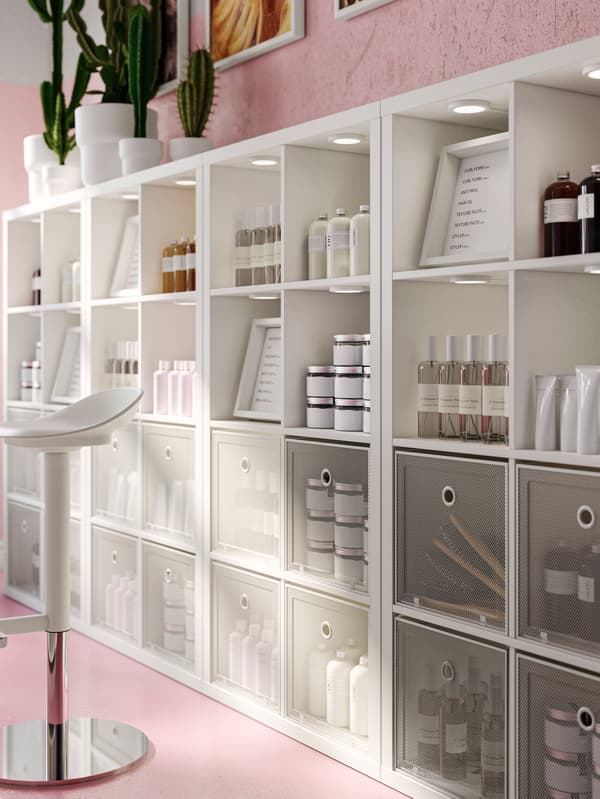 A number of white KALLAX shelving units, containing a variety of different items, stand against a wall.