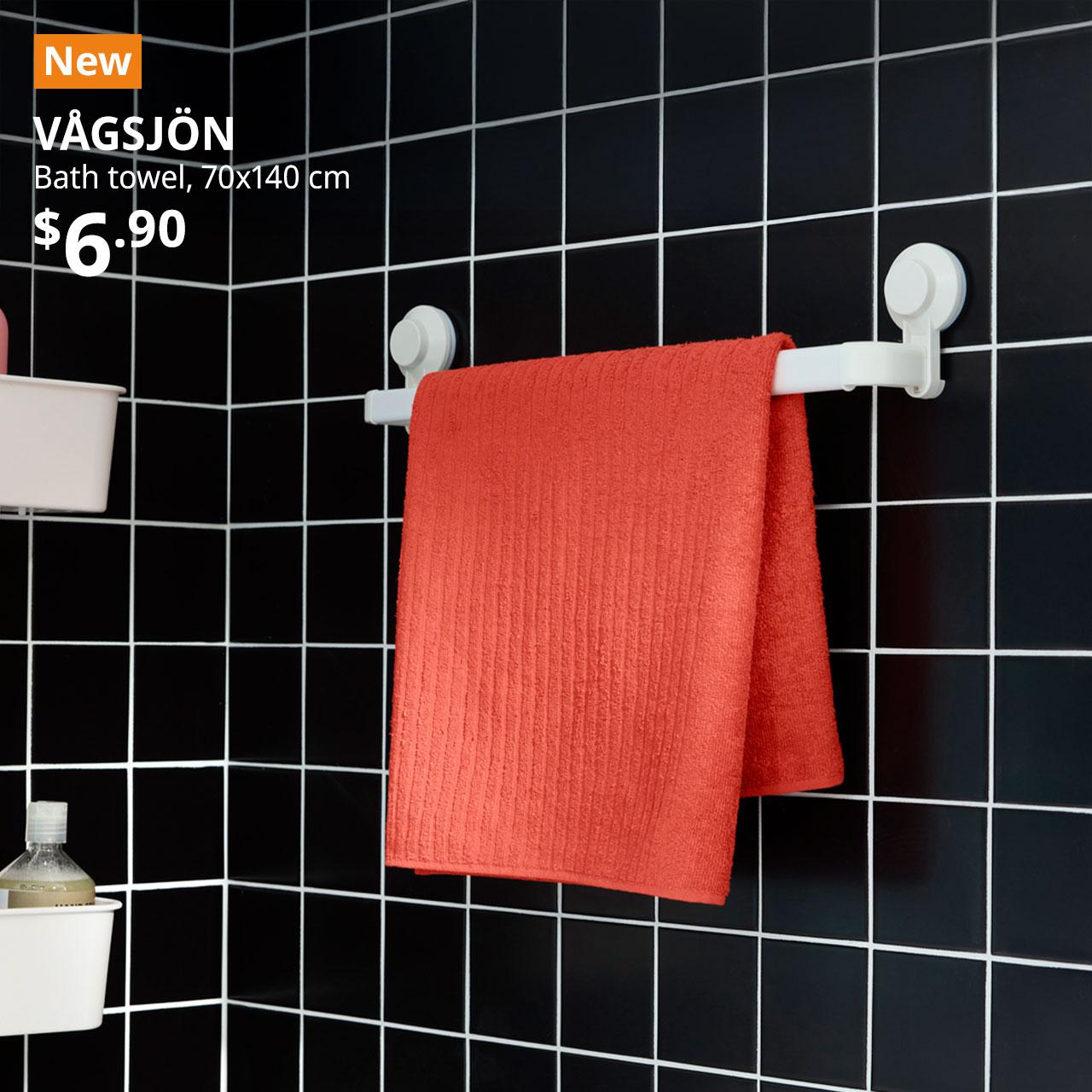 A orange-red VÅGSJÖN bath towel is placed on a white TISKEN towel rack with suction cup in a bathroom setting. Text on image reads "New, VÅGSJÖN, Bath towel, 70x140 cm, $6.90"