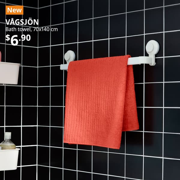 A orange-red VÅGSJÖN bath towel is placed on a white TISKEN towel rack with suction cup in a bathroom setting. Text on image reads "New, VÅGSJÖN, Bath towel, 70x140 cm, $6.90"