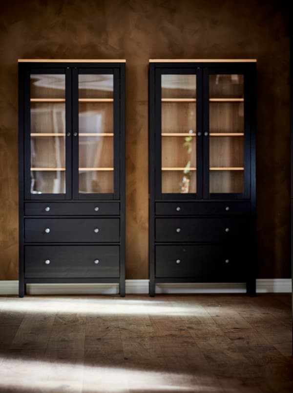 A pair of dark HEMNES glass-door cabinets standing empty against the brown wall of an otherwise empty room.