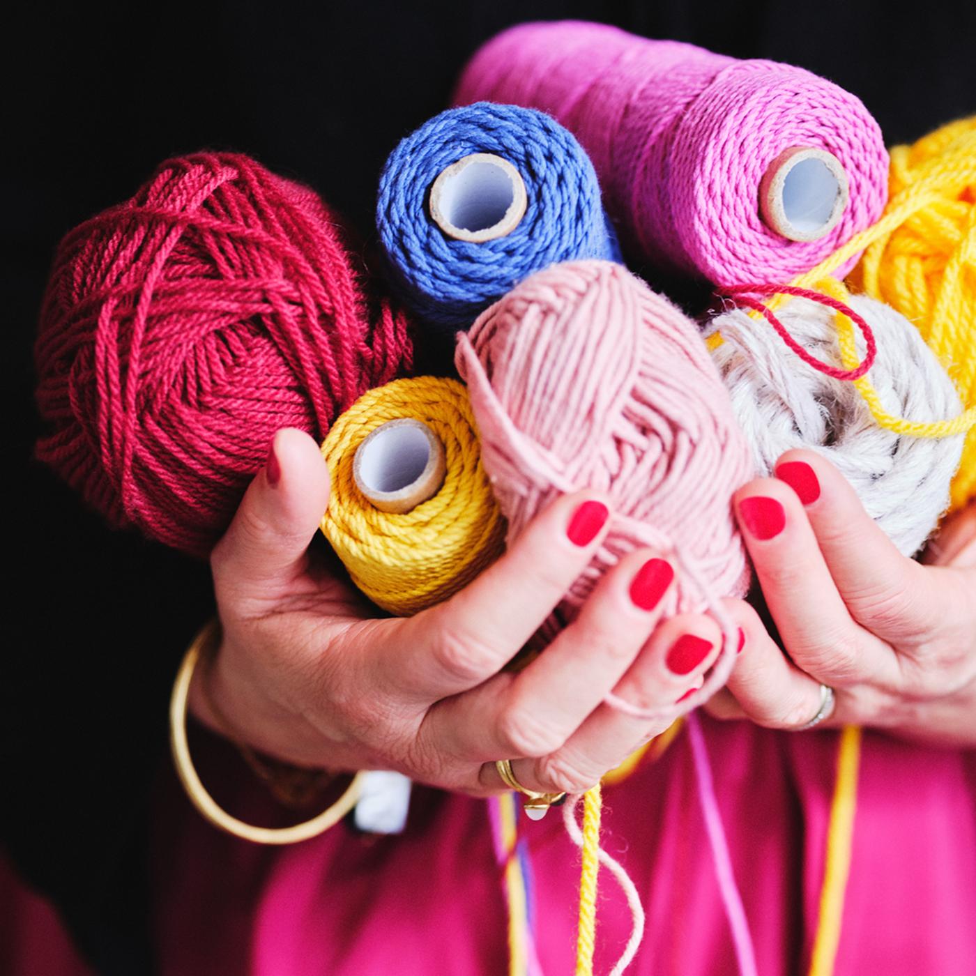 A pair of hands holding colorful spools of thread and balls of yarn.