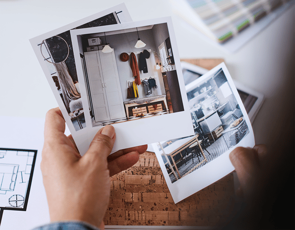 A pair of hands holding up photographs of the interior of a home, to illustrate IKEA home design service