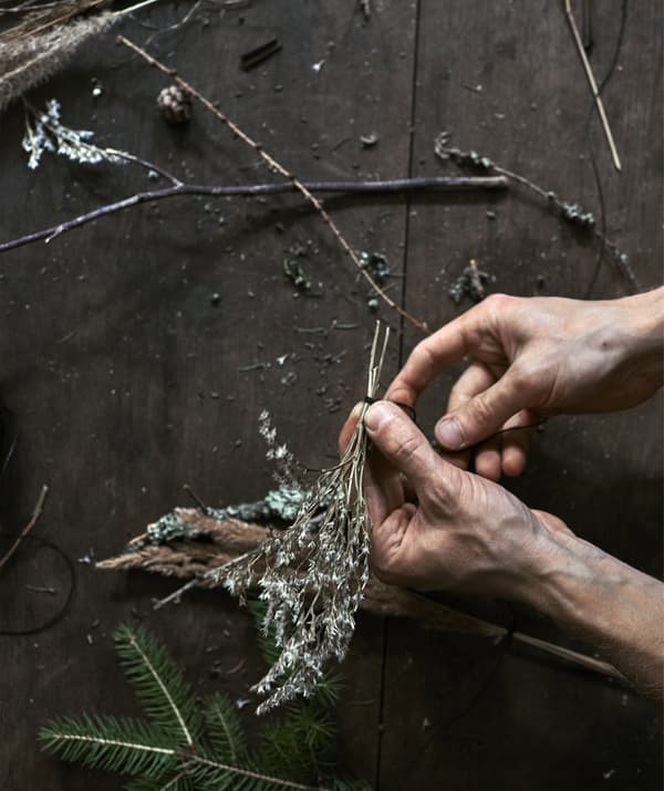 A pair of hands tying a green sprig with black thread
