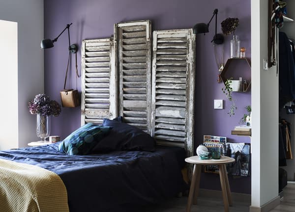 A pair of old white farmhouse shutters that have been re-purposed into a headboard above a bed.