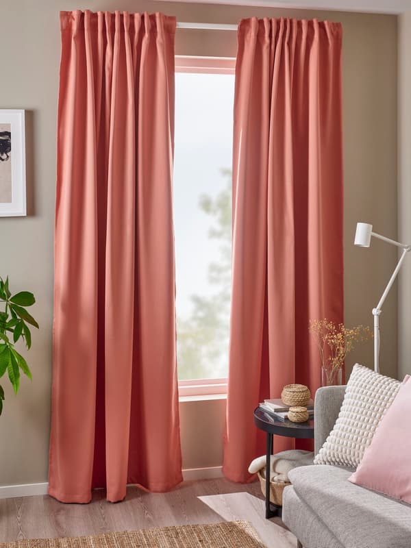 A pair of pink MAJGULL room dark curtains are hung in the living room in front of a full window, beside a plant and a picture frame.