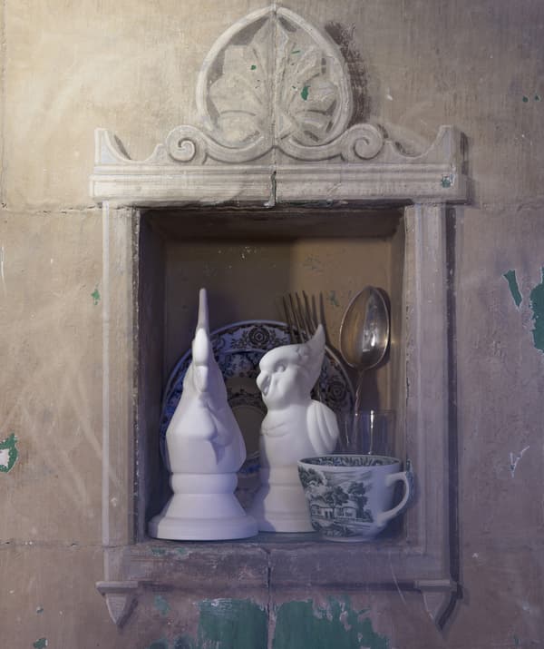 A pair of white bird ornaments and some tableware in the nook of a wall.