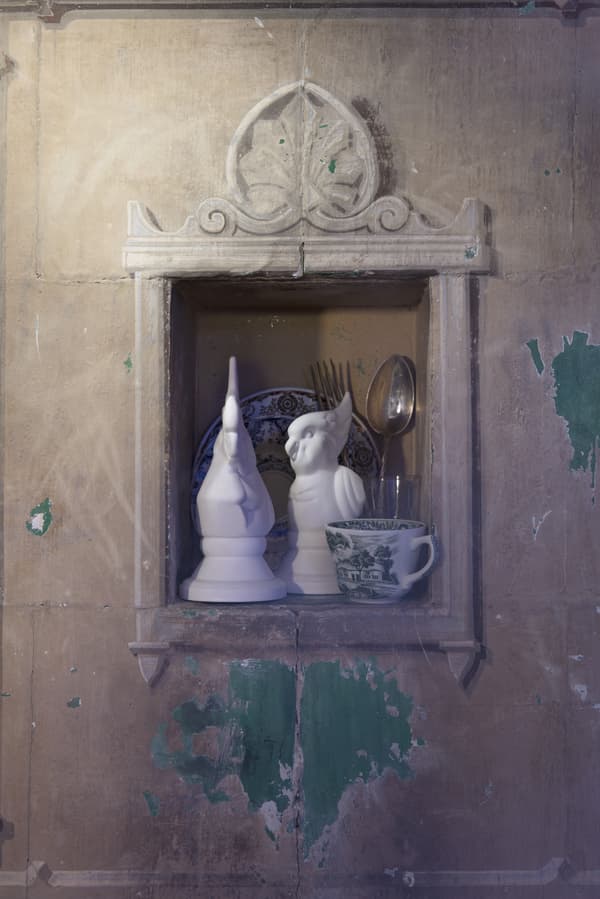 A pair of white bird ornaments and some tableware in the nook of a wall.
