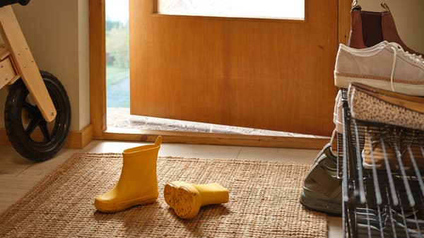 A pair of yellow children’s boots lie on a LOHALS flatwoven rug in a hallway next to a partly open front door.
