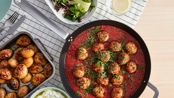 A pan with mince balls, made from VÄRLDSKLOK plant-based mince, in tomato sauce and an oven tray with roasted potatoes.