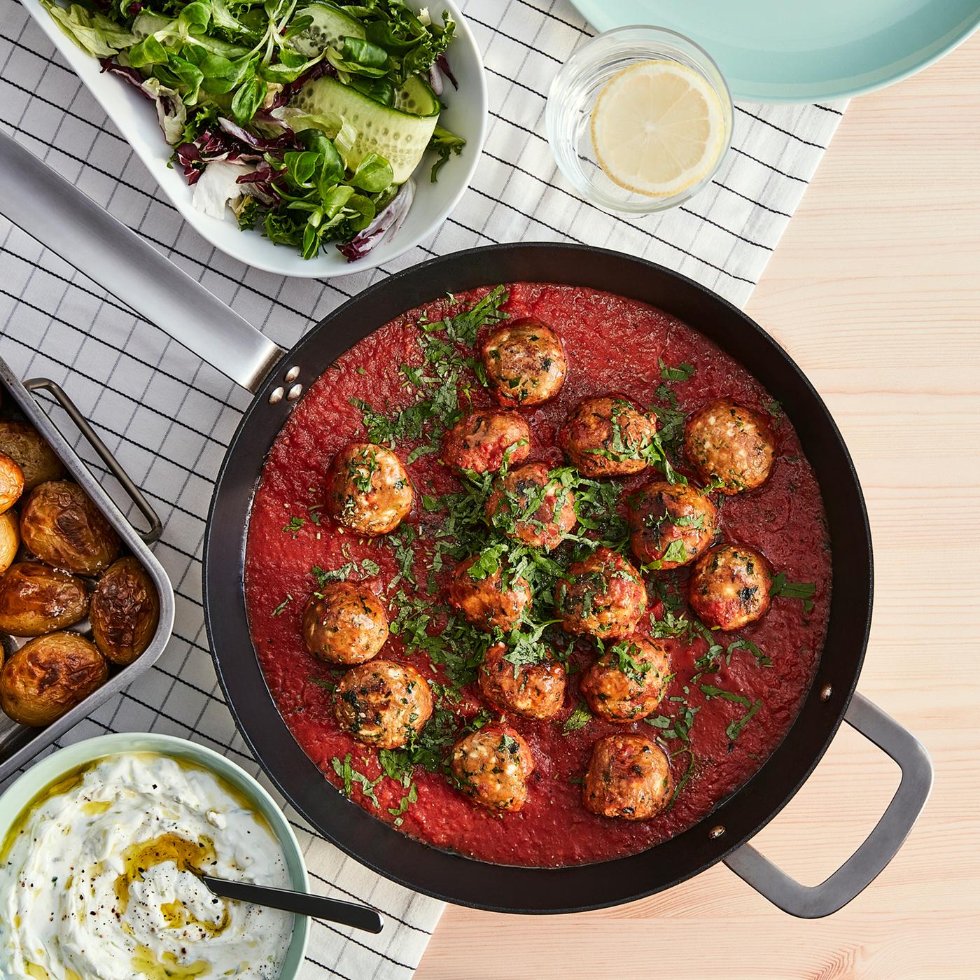 A pan with mince balls, made from VÄRLDSKLOK plant-based mince, in tomato sauce and a roasting tin with roasted potatoes.