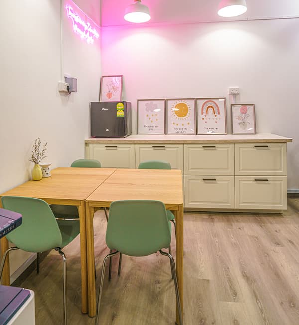 A pantry area featuring wooden tables, green chairs and a white cabinet placed against a wall.