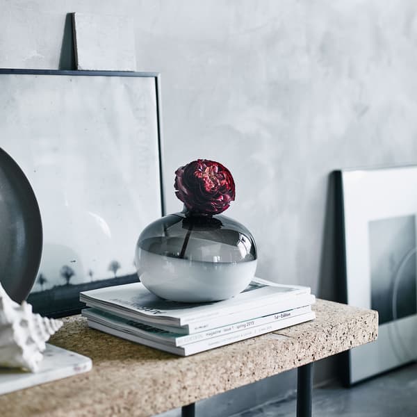 A paper rose in a black and white glass vase on a cork shelf.