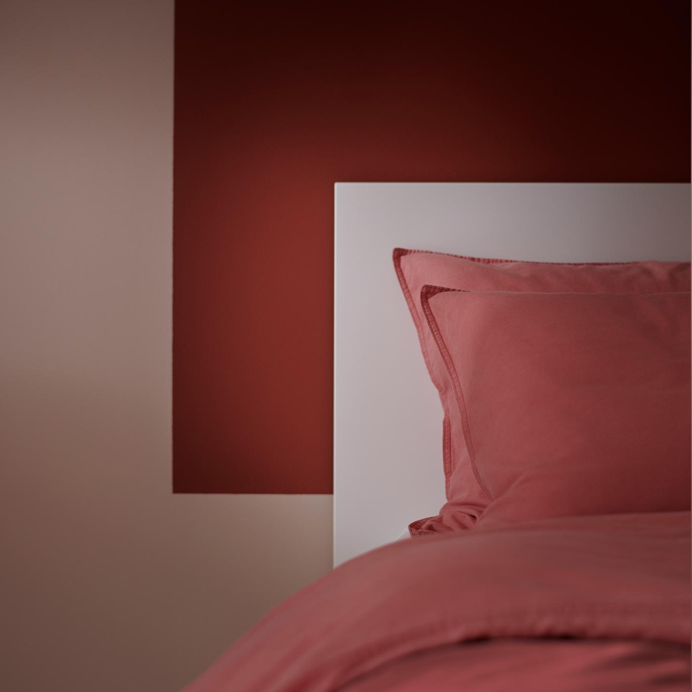 A part of a bed with light brown-red ÄNGSLILJA bed linen stands against a wall partly painted in a matching brown-red.