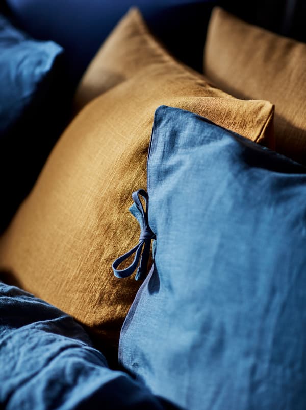A parte de uma cama, onde a capa de edredão se junta às almofadas, feita com elegância e simplicidade com roupa de cama PUDERVIVA em azul, combinada com duas almofadas em açafrão escuro.
