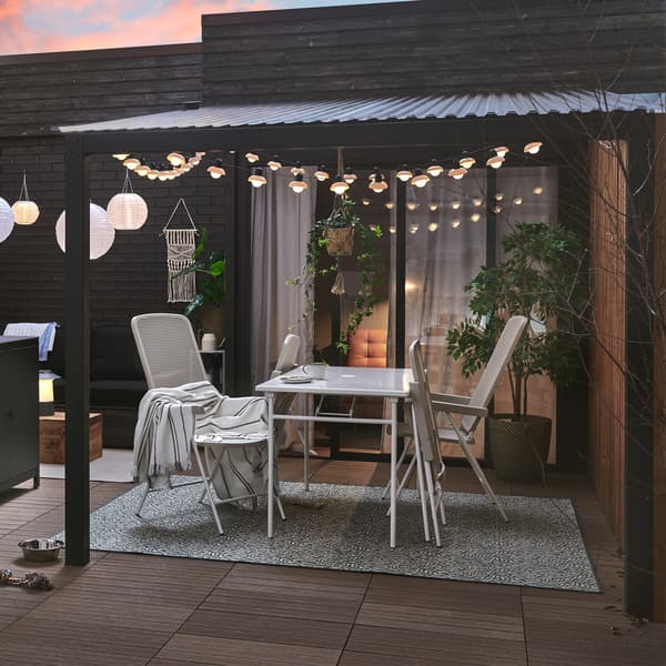 A patio set up with a GRILLSKÄR charcoal grill and kitchen island, TORPARÖ table and chairs, and lights.