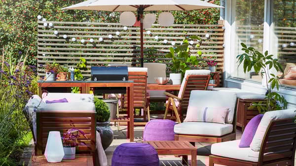 A patio with a barbecue, a 4-seat conversation set, a beige umbrella, purple pouffes and beige outdoor cushions.