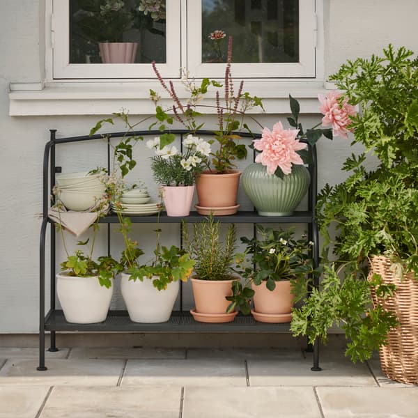 A patio with a grey LÄCKÖ shelving unit made for outdoor use, displaying various potted plants and flowers.