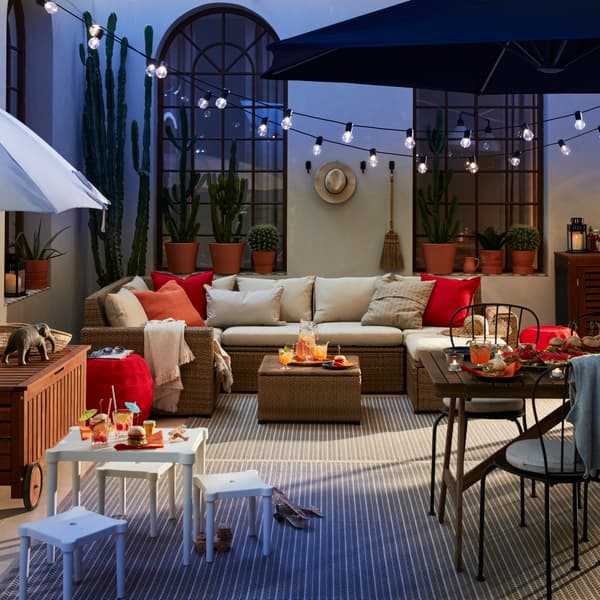 A patio with outdoor sofa and a smaller white table and stools, a dining table with chairs and a parasol.