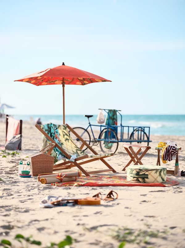 A patterned beach chair with an umbrella and towels, standing on a sandy beach. A blue bicycle stands in the background.