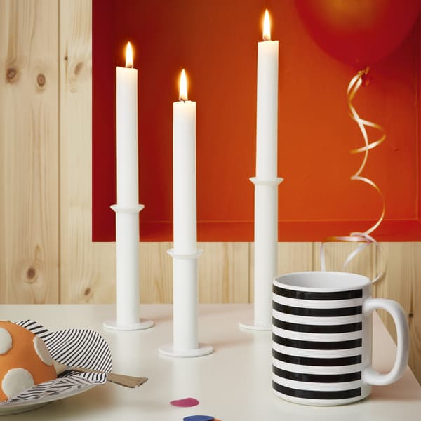 A patterned mug and three white candlesticks on a table in a wood-panelled room.