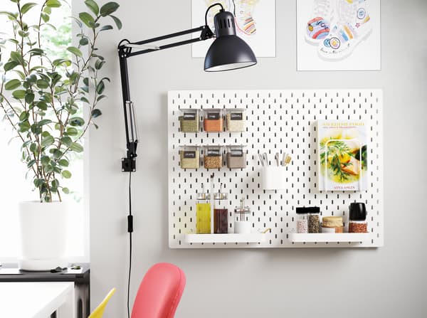 A pegboard mounted on a wall next to a dining table. The pegboard has accessories that store oils, seasonings and a cookbook.