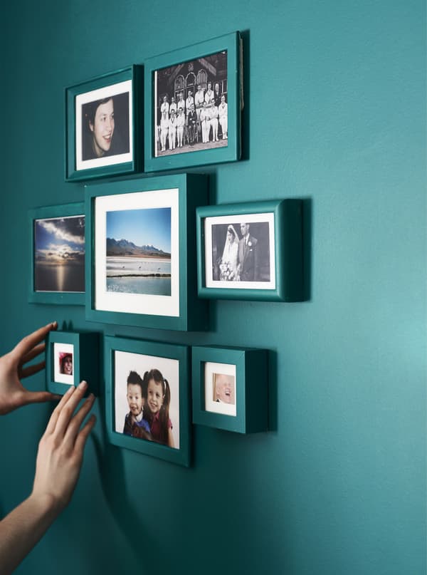 A person adding the final frame to a gallery wall of personal photos.