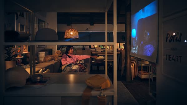 A person and a dog lying on a JÄTTEBO 3-seat modular sofa watching a show projected on a white TRETUR block-out roller blind.