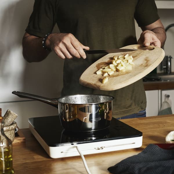 A person cooking on a portable induction cooktop, putting vegtables into a pot.