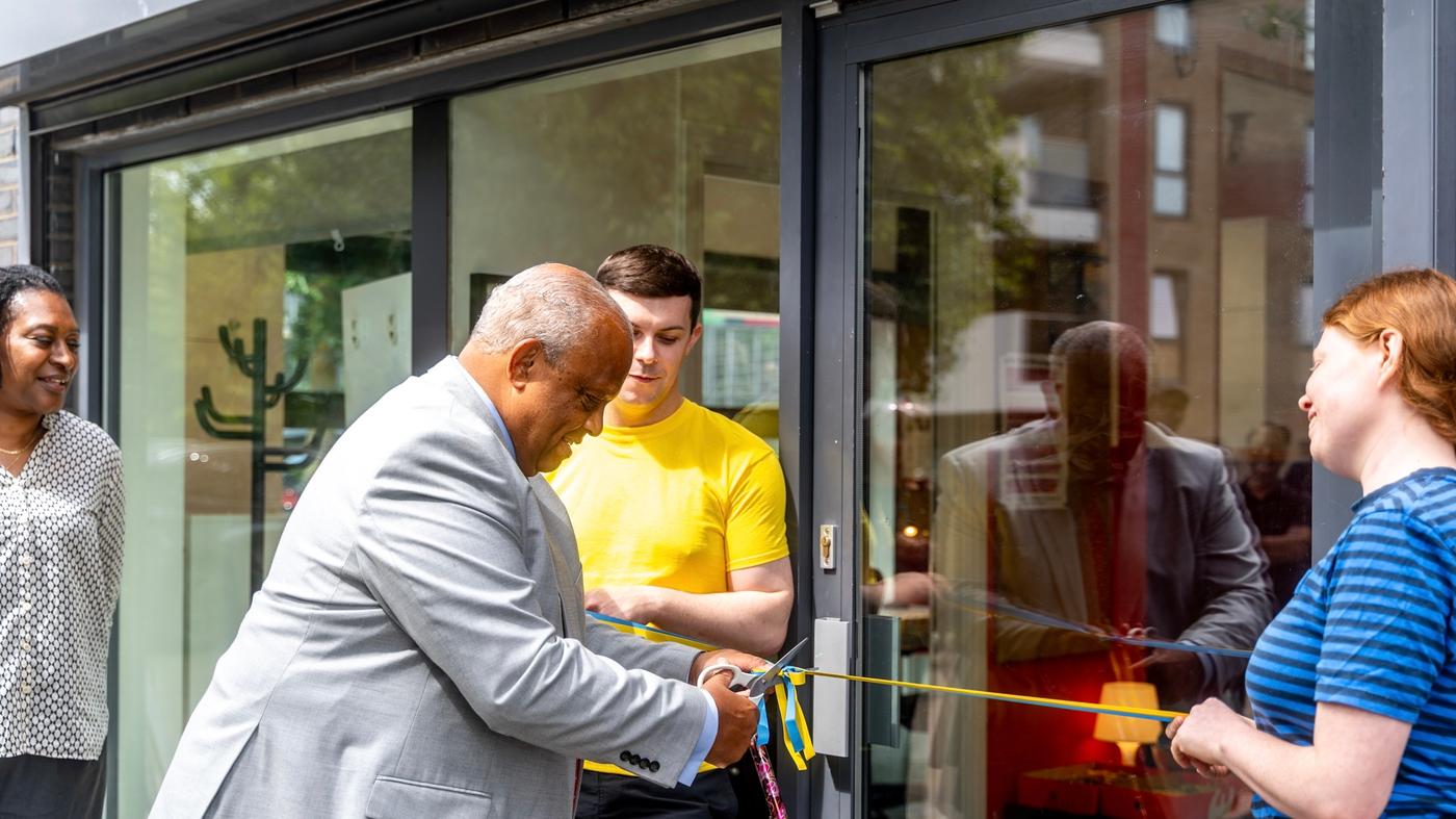 A person cutting a ribbon in front of a store for the opening. Two IKEA co-workers stand on the sides of a shop window.