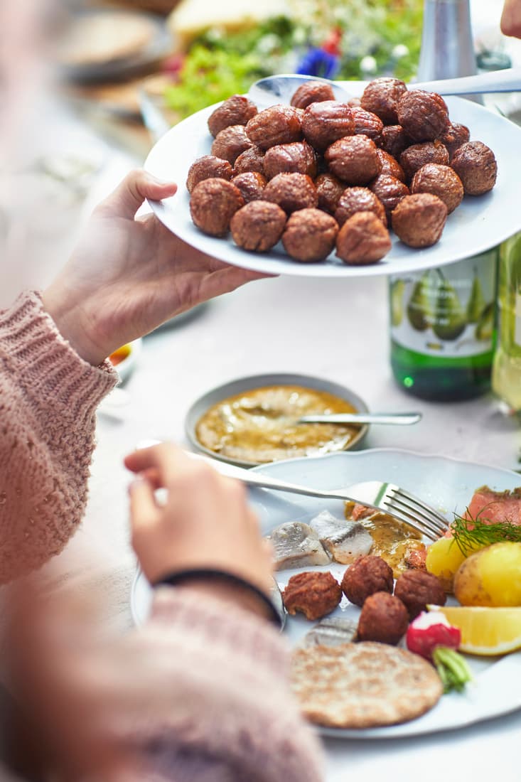 A person handing out a plate of meatballs at a festive table filled with various food items.