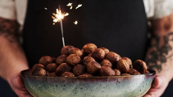 A person holding a large bowl filled with meatballs and a sparkler sticking out of it