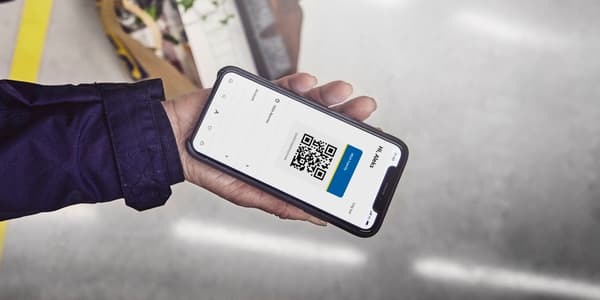 A person holding a mobile phone showing a QR code for IKEA Family loyalty club.