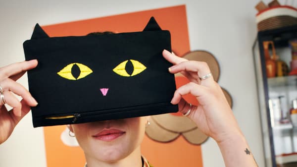 a person holding a pouch in the shape of a black cat in front of their eyes