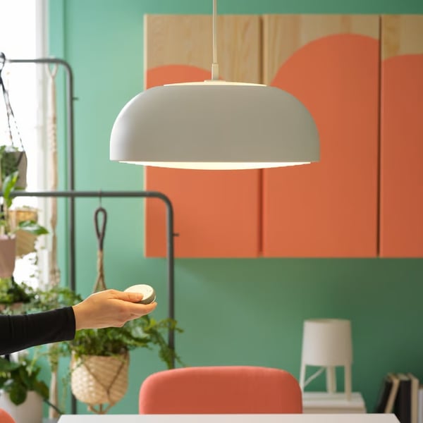 A person holding a small remote control beneath a pendant lamp in a colourful room with green walls and orange cabinets.