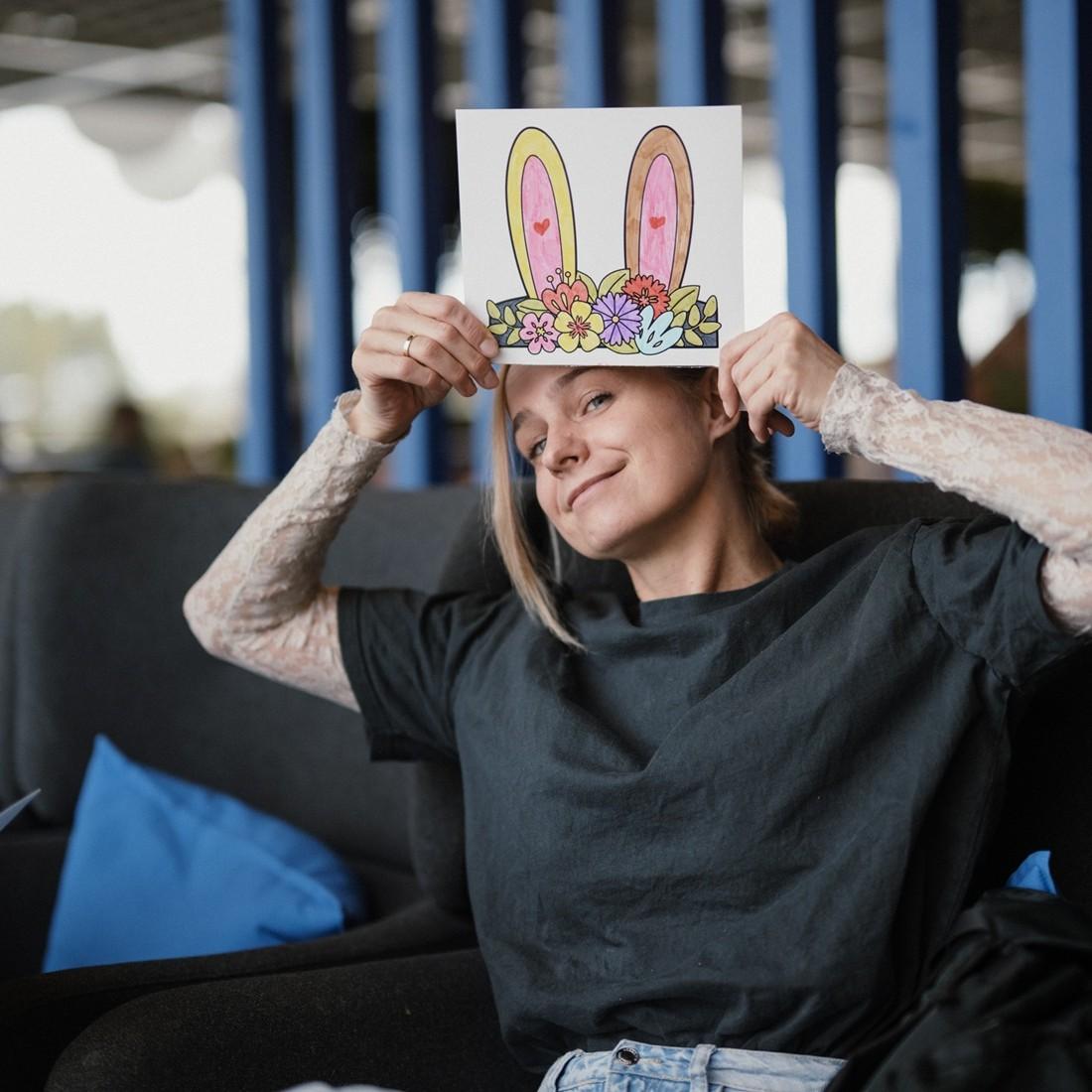 A person holds a sheet of paper with illustrated bunny ears above their head, smiling playfully.