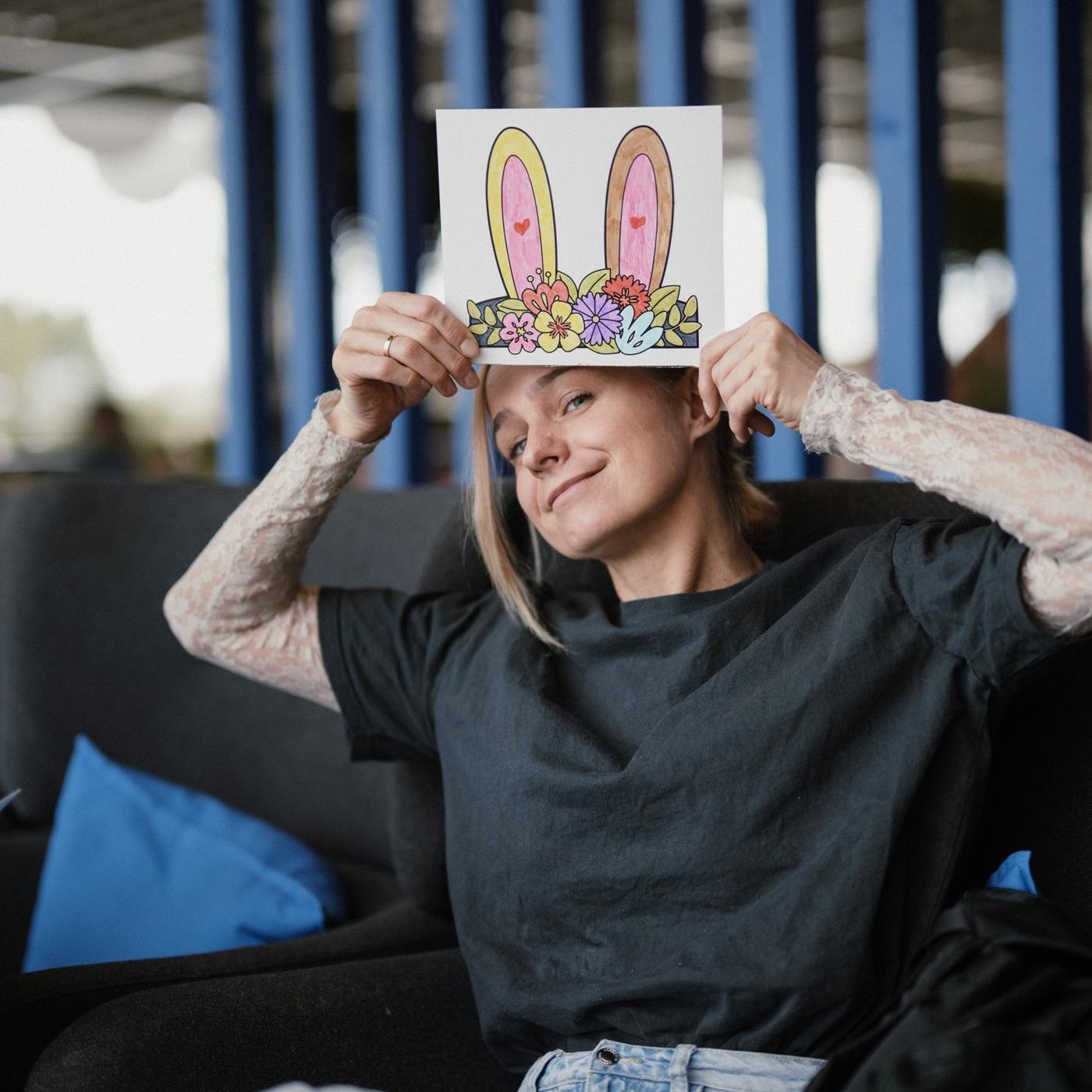 A person holds a sheet of paper with illustrated bunny ears above their head, smiling playfully.