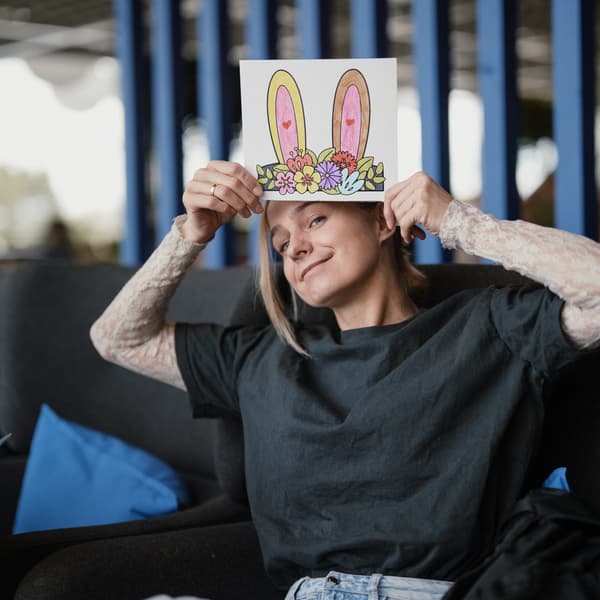 A person holds a sheet of paper with illustrated bunny ears above their head, smiling playfully.