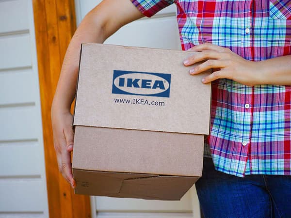 A person in a bright plaid shirt, carrying a box with an IKEA logo.