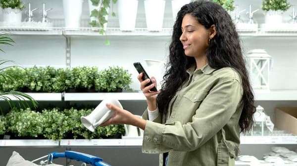 A person in a store is holding a phone and a white flower pot.