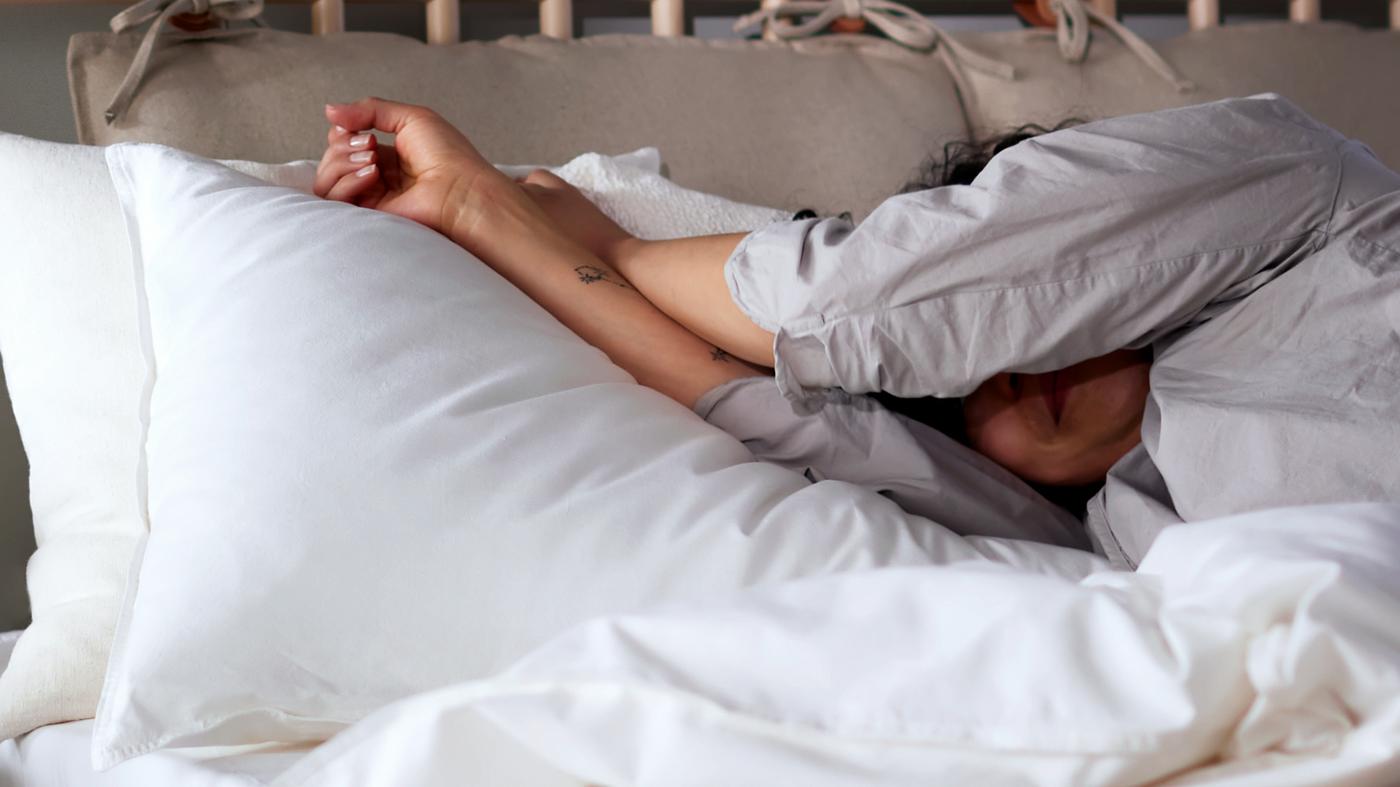 A person in pajamas lying in a birch BJÖRKSNÄS bed made with white ÄNGSLILJA bed linen.