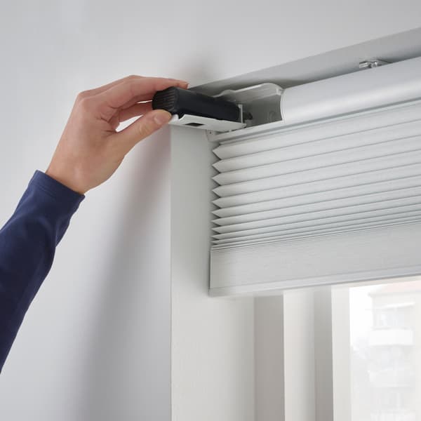 A person installing a white blind onto a window.