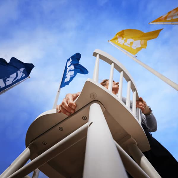 A person is carrying a chair outdoors, surrounded by IKEA flags. 