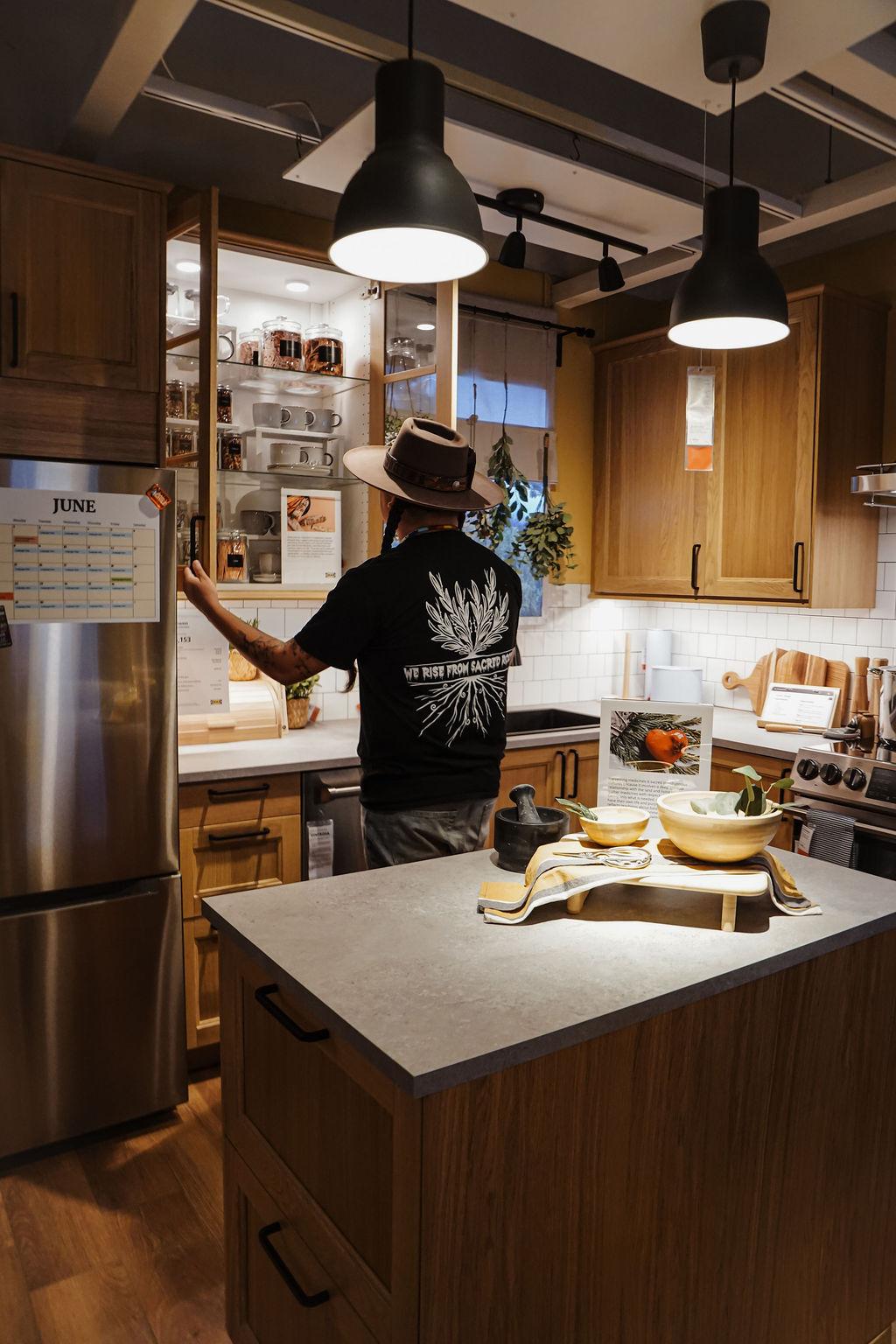 A person is in a kitchen opening a kitchen cupboard and looking at the contents inside.