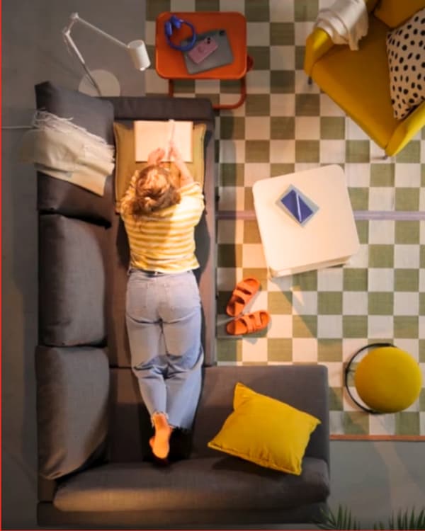 A person is lying comfortably on a grey couch with a book, surrounded by colorful furniture and accessories.