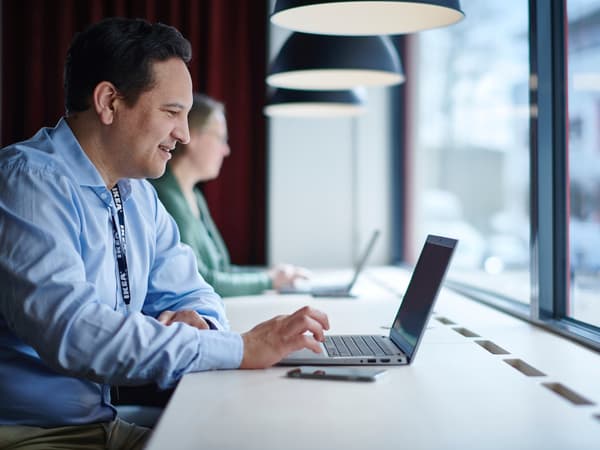 A person is sitting at a desk with an open laptop in front of them and a large window behind them.