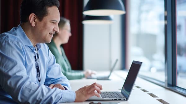 A person is sitting at a desk with an open laptop in front of them and a large window behind them.