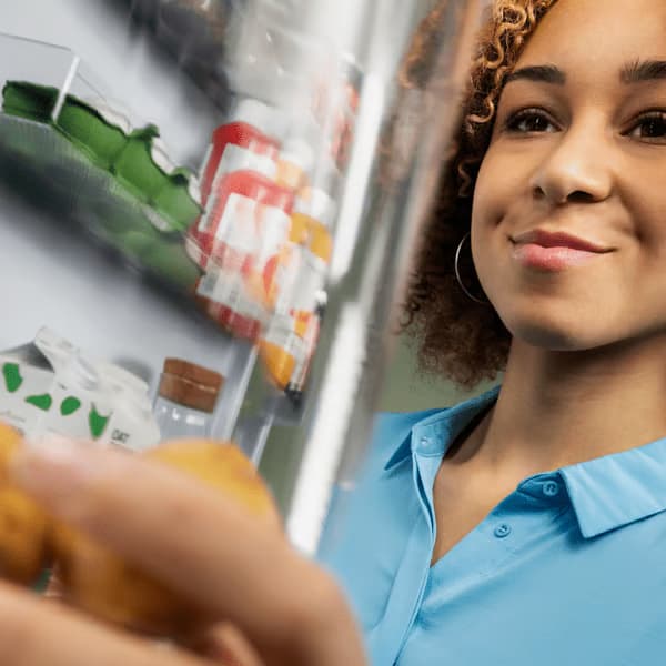 A person is smiling while reaching into a refrigerator to pick up something up.